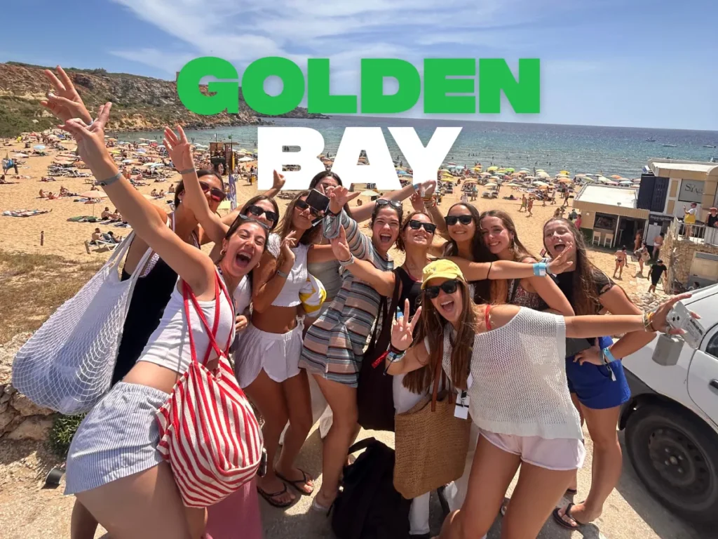 Grupo de jóvenes en la playa de Golden Bay, Malta, con arena dorada y agua turquesa