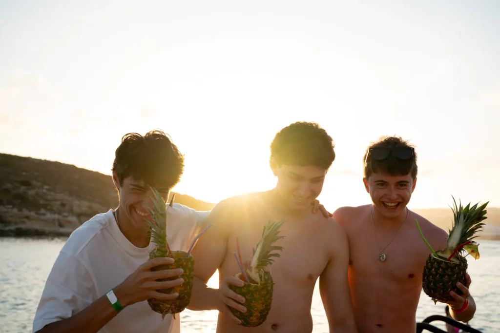 Tres chicos con piñas de cóctel al atardecer en Comino en su viaje de fin de carrera a Malta
