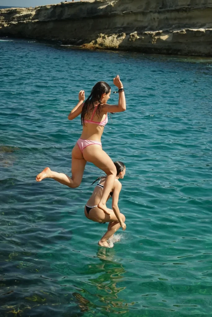 Dos chicas saltando desde las rocas al agua turquesa en Malta en su viaje después de selectividad